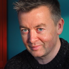 A fairskinned man with short hair indoors illuminated by natural light.