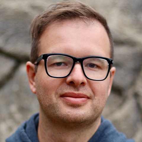 A man with short hair and glasses with a neutral expression on his face.