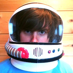 The eyes of a man with an impressive foppish fringe look out from inside a brightly-coloured child's space helmet.
