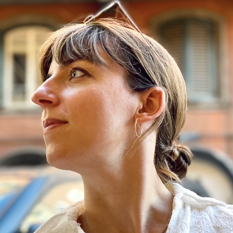 A profile of a woman outdoors with her hair tied back and glasses on her head as she looks into the distance.